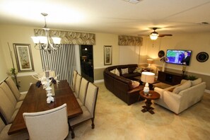 A living room with a dark brown sofa, a beige sofa, a dining table with chairs, and a TV mounted on the wall. - Ov4182 - Champions Gate Resort - 8 Bed 5 Baths Villa (Davenport)