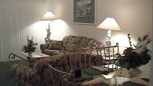 Een woonkamer met een gestreept bankje, twee lampen, een glazen salontafel en een lijst met een afbeelding aan de muur.