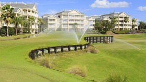 Un parcours de golf doté d’un grand club-house comprenant de nombreux balcons et des palmiers.