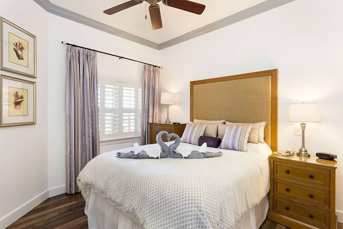 Un dormitorio ordenado con una cama grande, cabecera de madera, una mesita de noche con lámpara y ventilador de techo.