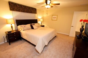 A bedroom with a bed, two bedside tables, a ceiling fan, a lamp, a framed picture, and a door.