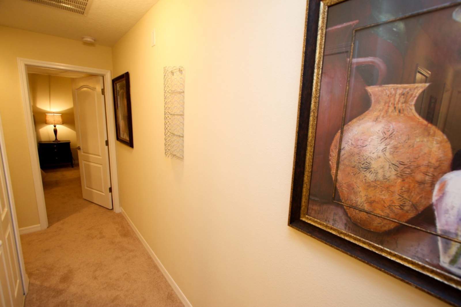 A hallway with a carpeted floor, a door leading to another room, and a framed picture on the wall.