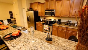 A kitchen with granite countertops, wooden cabinets, a stainless steel refrigerator, a microwave, a stove, and a coffee maker.