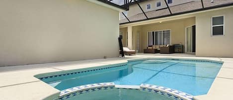Une piscine dont le carrelage présente un motif géométrique, entourée d’une terrasse couverte offrant une vue sur un immeuble d’habitation.