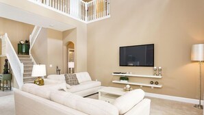 Een ruime woonkamer met een witte modulaire bank, een flatscreen televisie aan de muur en een trap met een witte leuning.