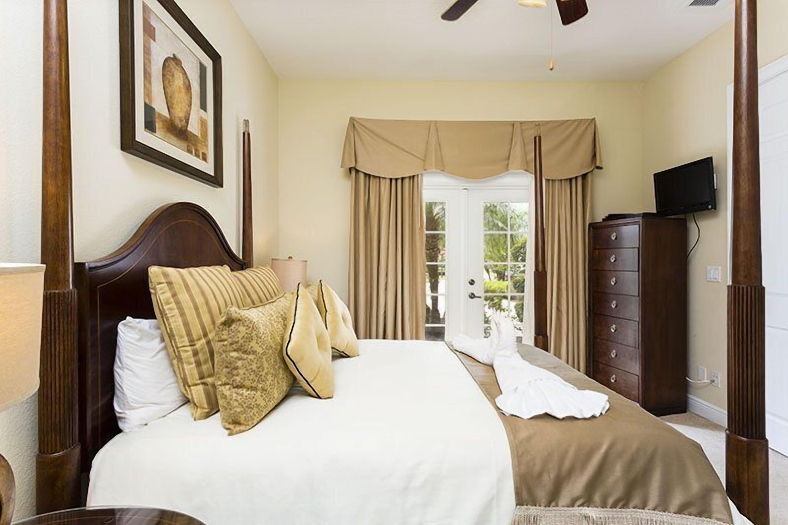 Une chambre à coucher bien rangée, avec un grand lit, une commode, un téléviseur et un ventilateur de plafond.