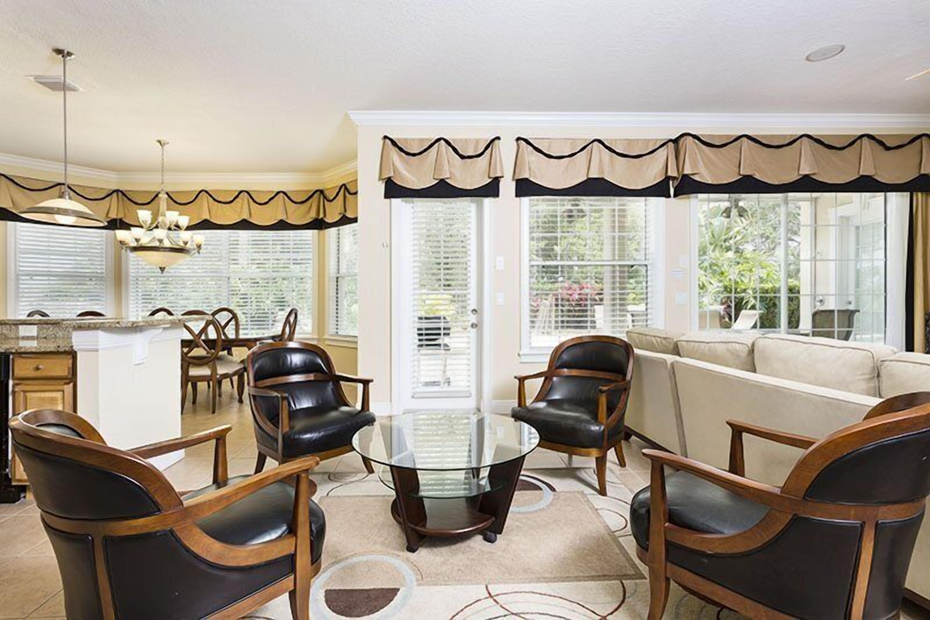 A spacious living room with a glass coffee table, leather chairs, and a beige sofa.