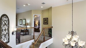 Una escalera con barandilla de madera y balaustres de metal negro, que conduce a un salón con un sofá y una lámpara.