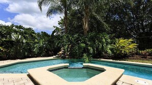 Una piscina con un jacuzzi en el centro, rodeada de exuberante follaje y palmeras.