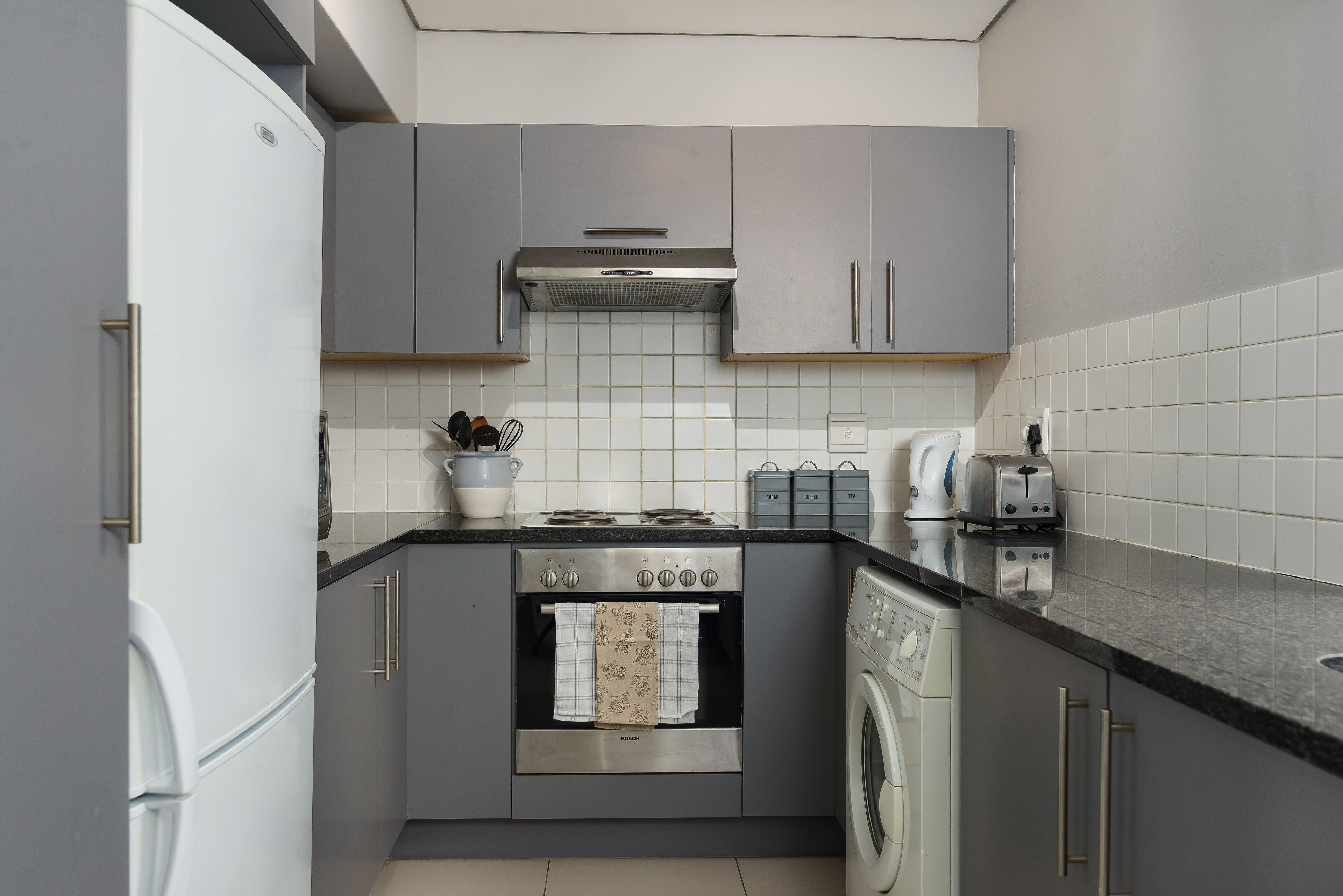A compact kitchen with grey cabinets, a Bosch oven, a washing machine, and a toaster.