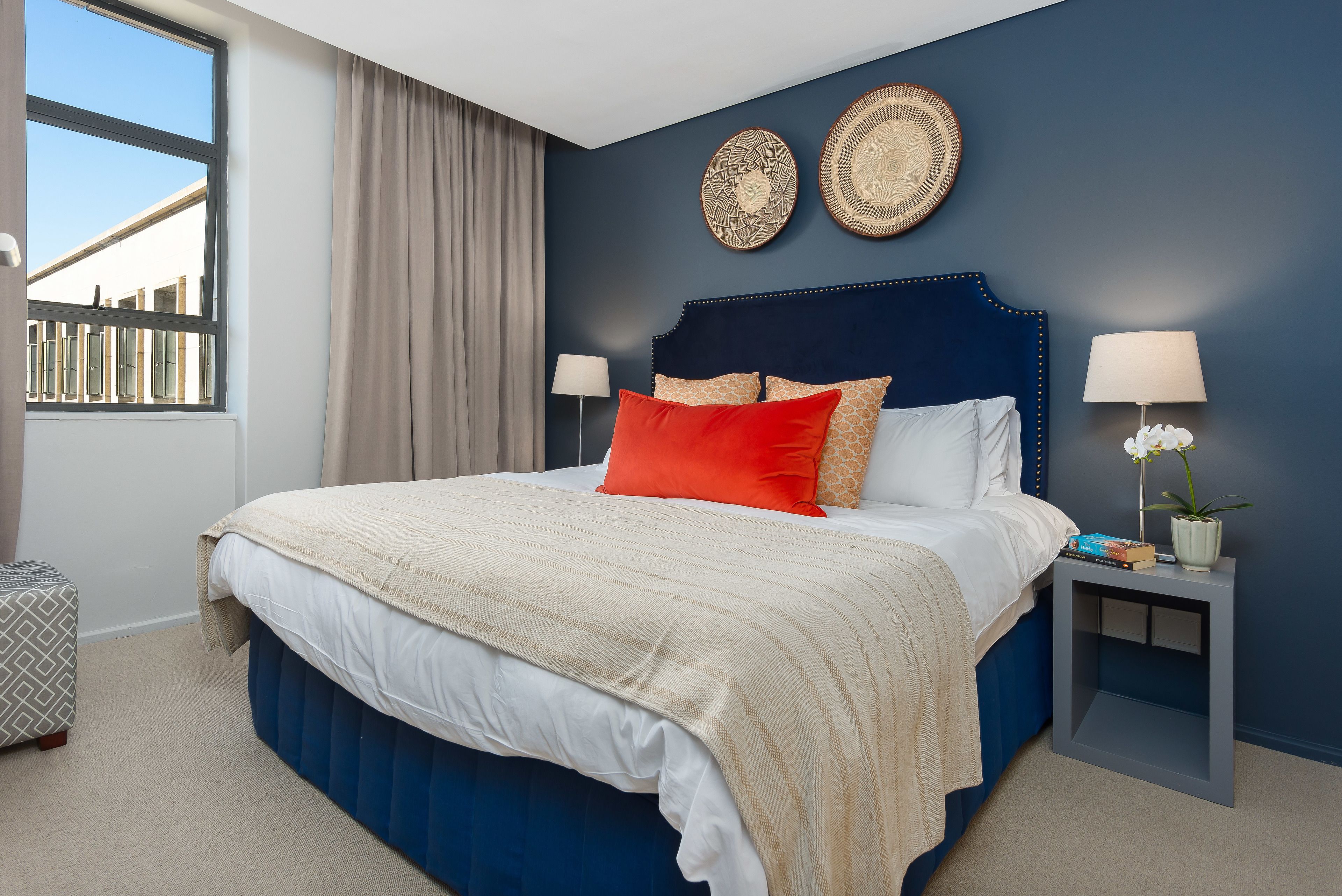 A modern bedroom with a large bed, two bedside tables, a window with curtains, and decorative wall art.
