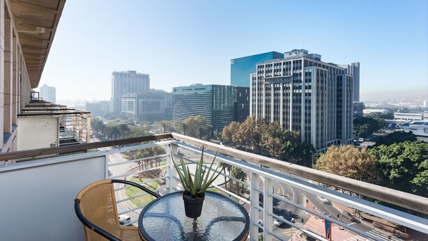 A balcony with a table and chair, a potted plant, and a cityscape view. - Fountain Suites 1001 (Cape Town)