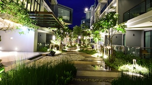Un pati d'hotel modern de nit amb camins il·luminats, elements aquàtics i vegetació abundant.