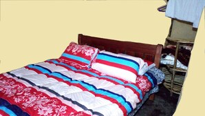 A bed with a striped and floral comforter, a wooden headboard, and a small wooden shelf with folded clothes. - Maverick Camp Rondavels and Homestay (Aberdare National Park)