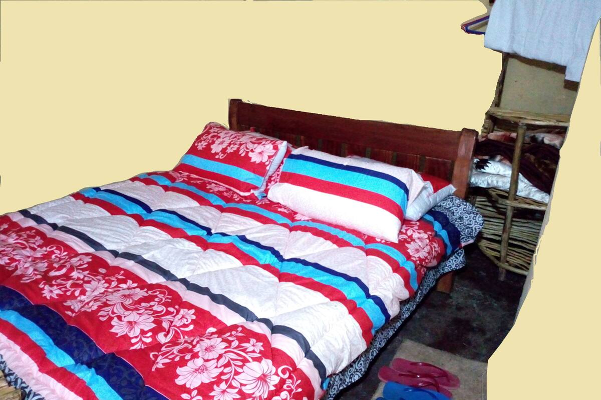 Una cama con edredón a rayas y con motivos florales, un cabecero de madera y un pequeño estante con ropa doblada.