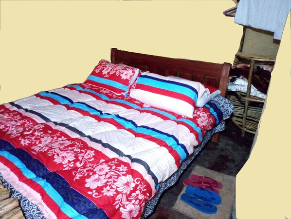 Una cama con edredón a rayas y con motivos florales, un cabecero de madera y un pequeño estante con ropa doblada.