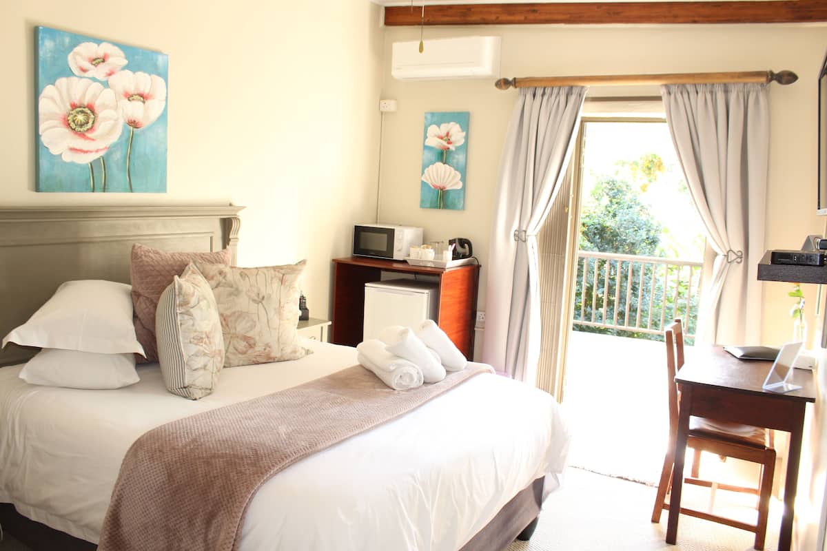 A hotel room with a bed, a desk, a chair, a microwave, and a small table with a laptop.