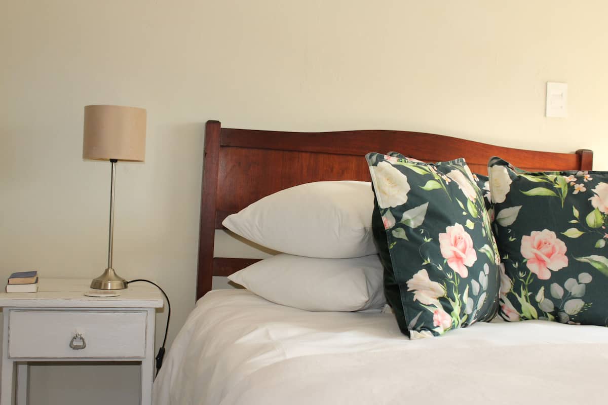 A neatly made bed with floral pillows, a bedside lamp, and a small bedside table with a book and a lamp.