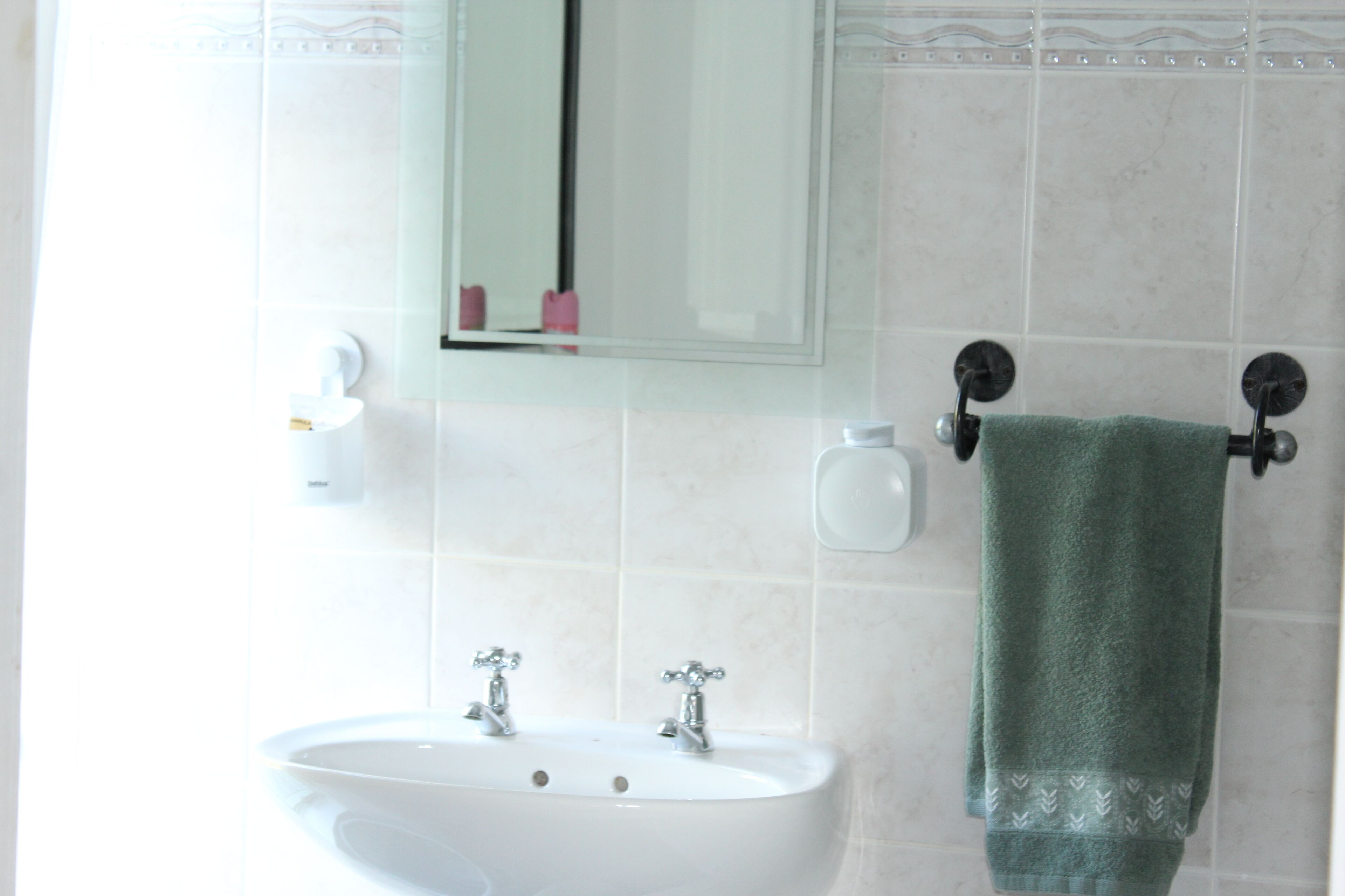 A bathroom with a white sink, two faucets, a mirror, and a towel rack with a green towel.