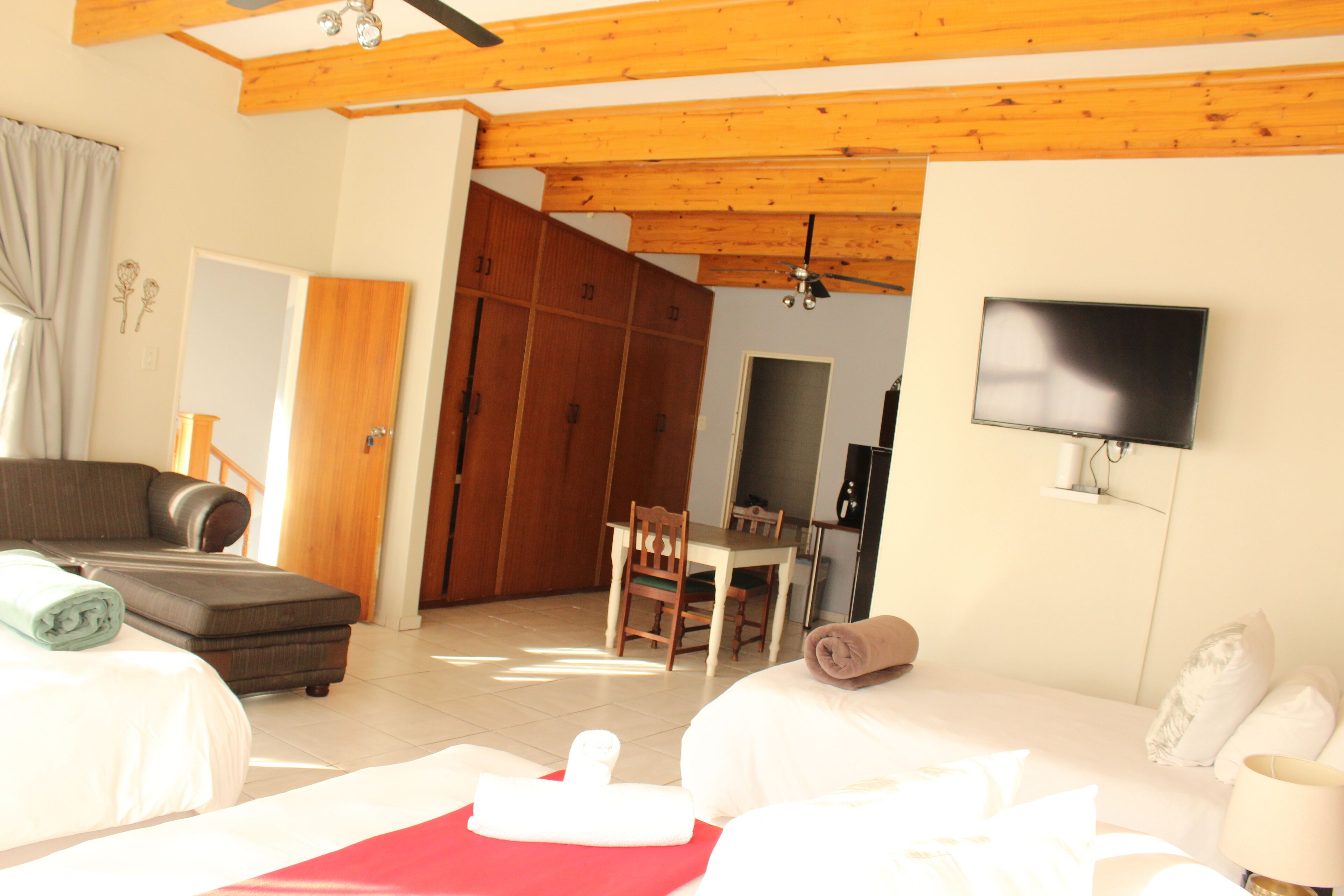 A hotel room with a bed, a sofa, a TV mounted on the wall, and a wooden ceiling.