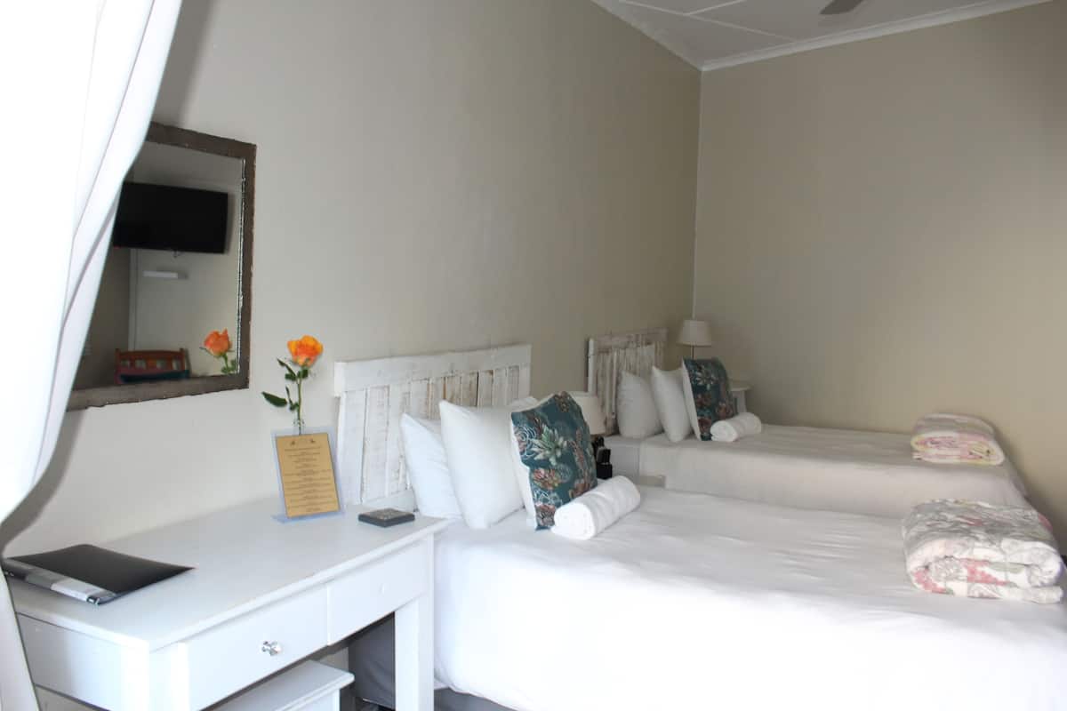 A hotel room with two beds, a desk, a chair, a TV, and a mirror.
