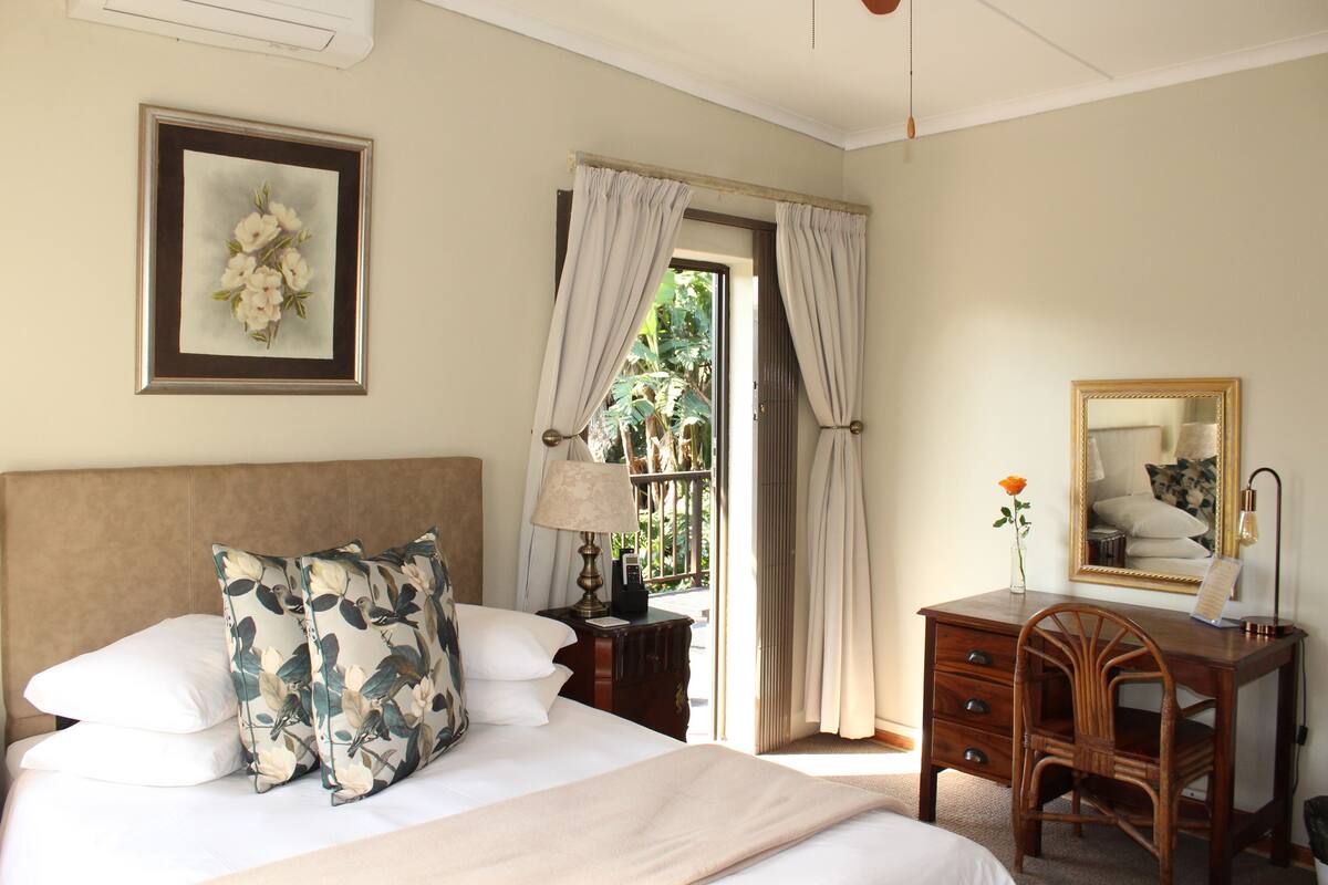 A bedroom with a bed, a desk, a chair, a mirror, and a window with curtains.
