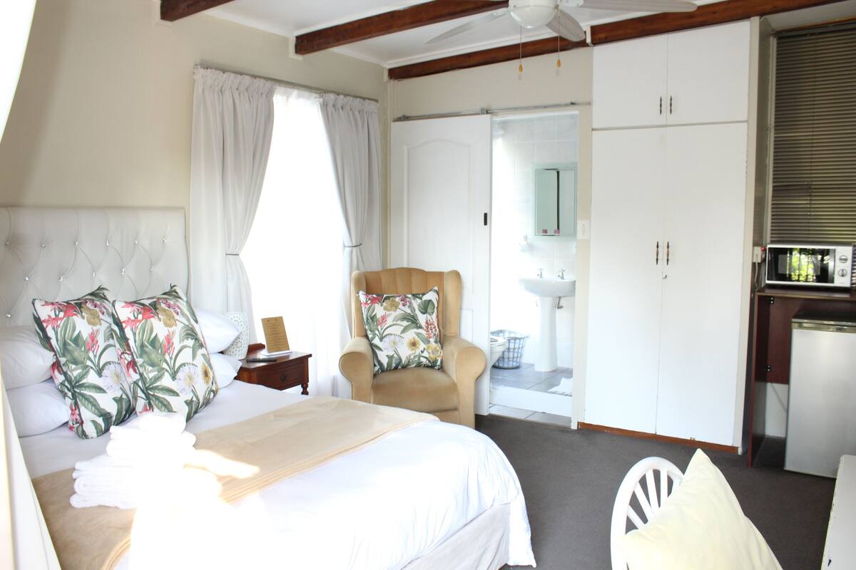 A hotel room with a bed, a chair, a desk, a wardrobe, and a bathroom visible through an open door.