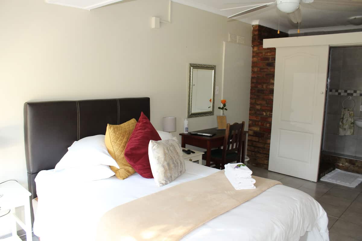 A hotel room with a bed, a desk, a chair, a mirror, and a door.