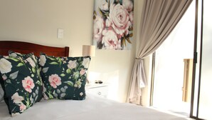 Un dormitorio con cama, almohadas estampadas, una mesita de noche, lámpara, un cuadro y ventana con cortinas.