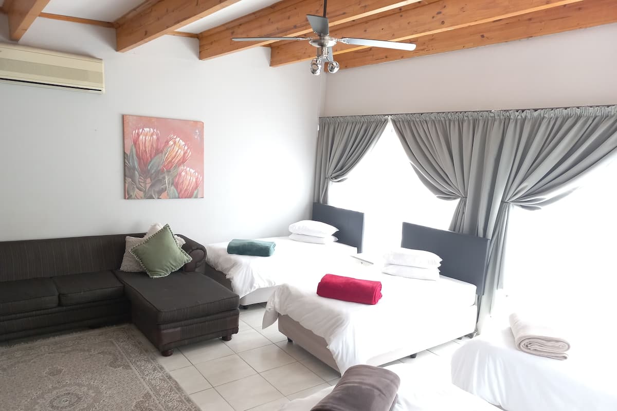 A hotel room with a bed, a sofa, a small table, and a ceiling fan.