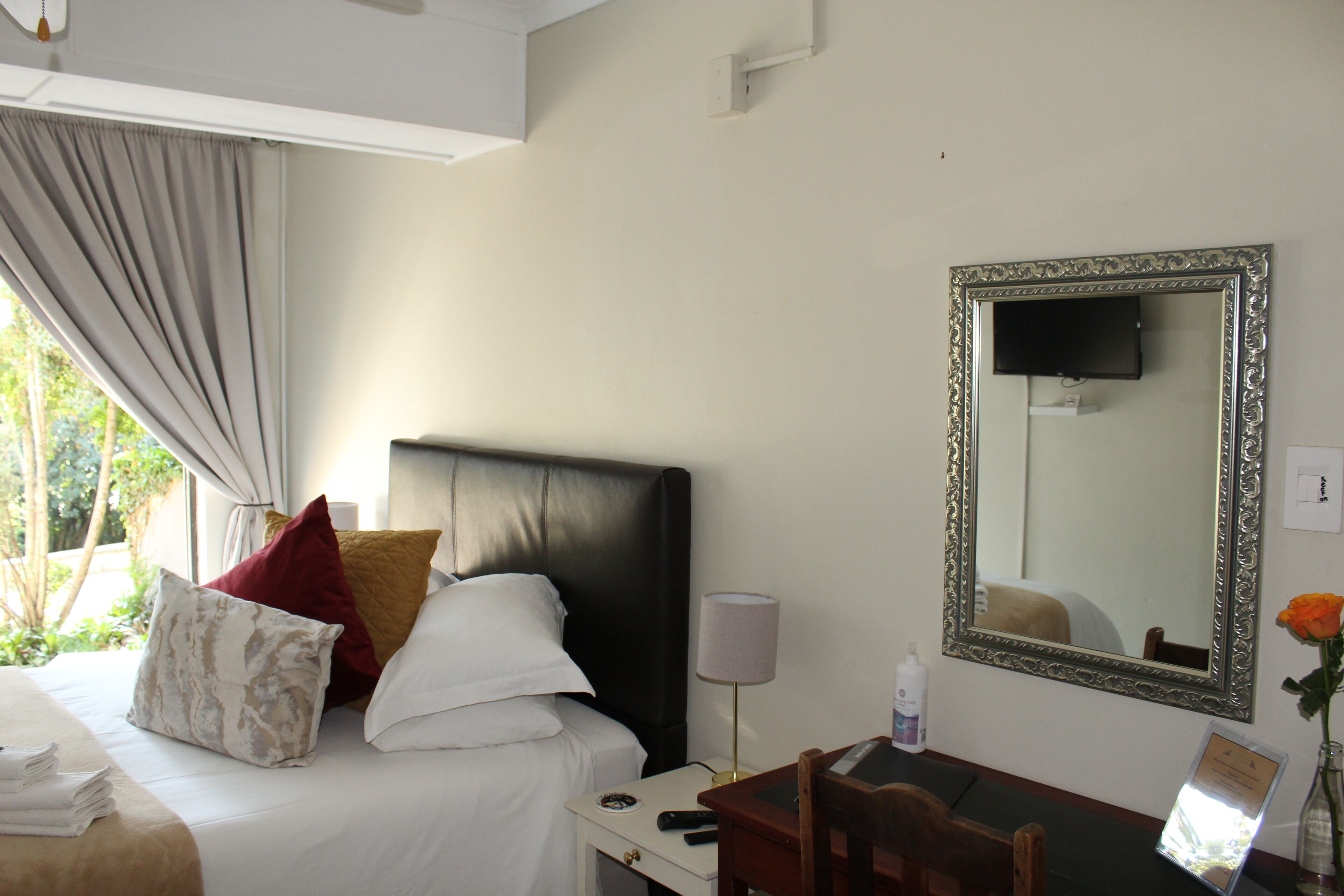 A hotel room with a bed, a desk, a chair, a lamp, a mirror, and a window with curtains.