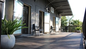 Un espacio al aire libre techado con terraza de madera, plantas en macetas y mobiliario exterior.