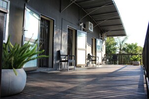 Uma área externa coberta com deck de madeira, plantas em vasos e mobiliário para o exterior.