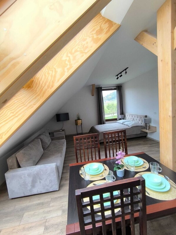 A loft-style bedroom with a sloped ceiling, a bed, a seating area, and a dining table set for two.