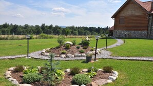 A log cabin with a stone foundation, surrounded by a well-maintained garden with a gravel path, various shrubs, and a few potted plants. - Agroturystyka Dom z Bali (Miłk ów)