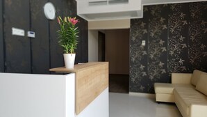 A modern reception area with a wooden reception desk, a potted plant, a clock, and a patterned wall. - Agroturystyka Dom z Bali (Miłków)