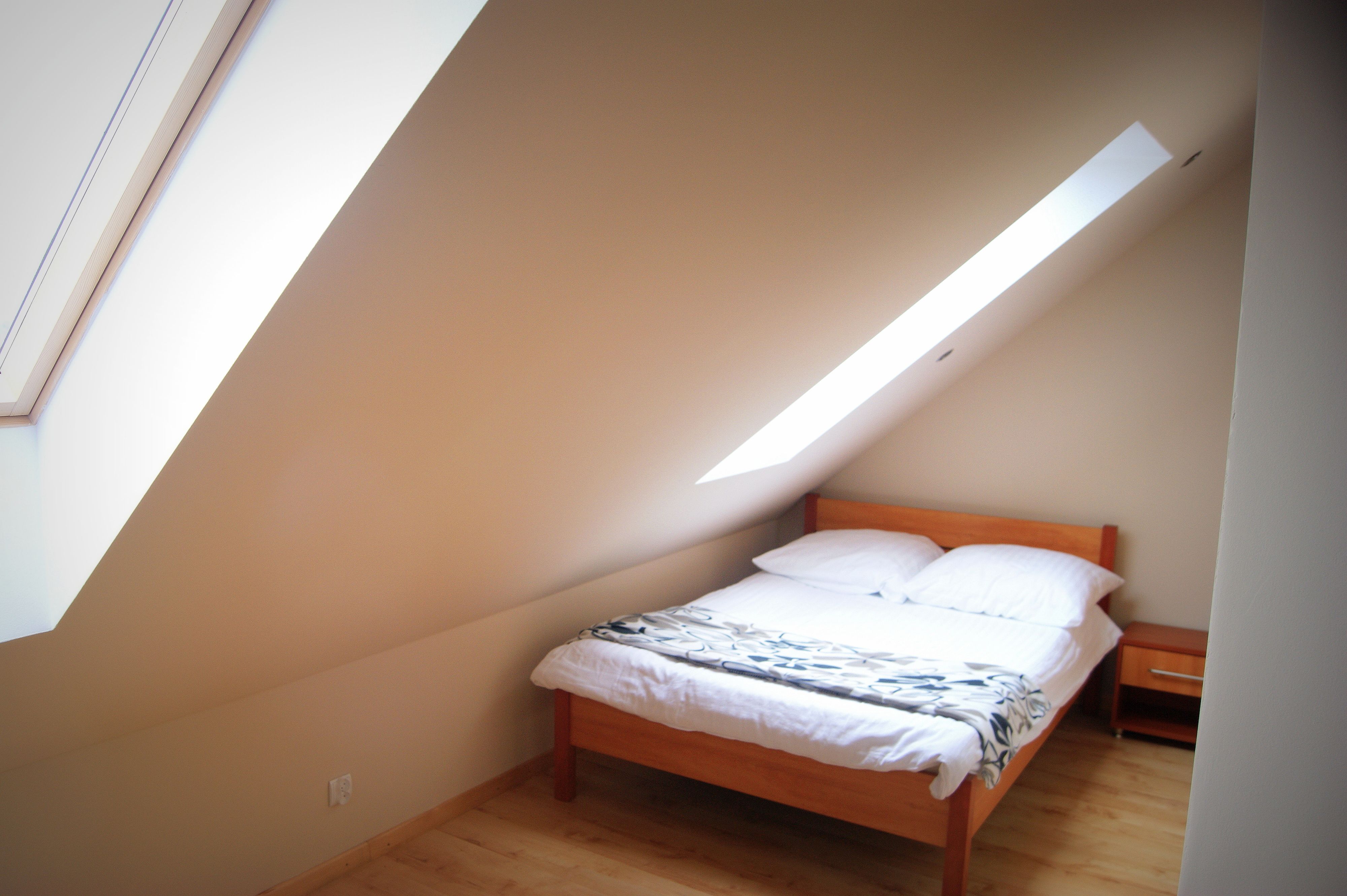 A bedroom with a sloped ceiling, a bed, a nightstand, and a skylight.