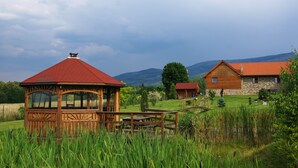 A wooden gazebo with a red roof, a stone building with a red roof, and a grassy field with mountains in the background. - Agroturystyka Dom z Bali (Miłków)
