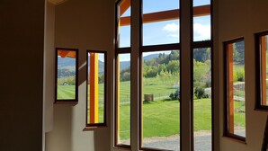A room with large windows offering a view of a green landscape with trees and a small building. - Agroturystyka Dom z Bali (Miłków)