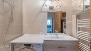 A modern bathroom with a glass shower enclosure, a built-in washing machine, a sink with a mirror, and a towel rack. - 2-room apartment in Megève, south-facing balcony, near center (Megève)