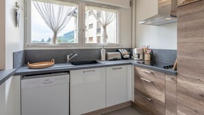 A modern kitchen with a dishwasher, a toaster, and a coffee maker. There are two windows with curtains, and a view of the outside. - 2-room apartment in Megève, south-facing balcony, near center (Megève)