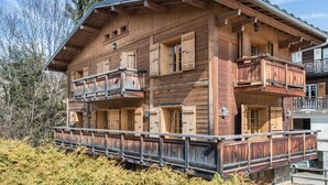 A wooden chalet with a balcony, a chimney, and a wooden deck.