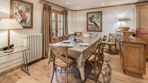 A dining room with a long table set for six, wooden chairs, a radiator, and a window with curtains.
