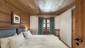 A bedroom with a wooden ceiling, a bed with white bedding, a framed picture on the wall, and a window with curtains.