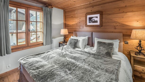 A cozy wooden room with a bed, two bedside tables, a window with curtains, and a framed picture on the wall.
