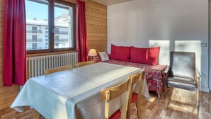 A cozy room with a wooden floor, a table with a tablecloth, a bed with red bedding, and a chair. - 2-room apartment with balcony and parking in Megève (Megève)