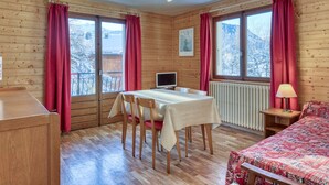 A cozy room with wooden walls, a bed, a table with chairs, a TV, and large windows with red curtains. - 2-room apartment with balcony and parking in Megève (Megève)