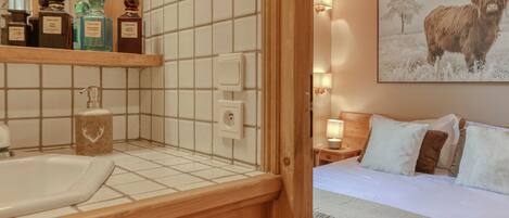 A hotel room with a wooden headboard, a bed with white bedding, a nightstand with a lamp, and a wall-mounted shelf with toiletries.