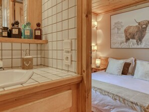 Ein Hotelzimmer mit einem hölzernen Kopfteil, einem Bett mit weißer Bettwäsche, einem Nachttisch mit Lampe und einem Wandregal mit Toilettenartikeln.