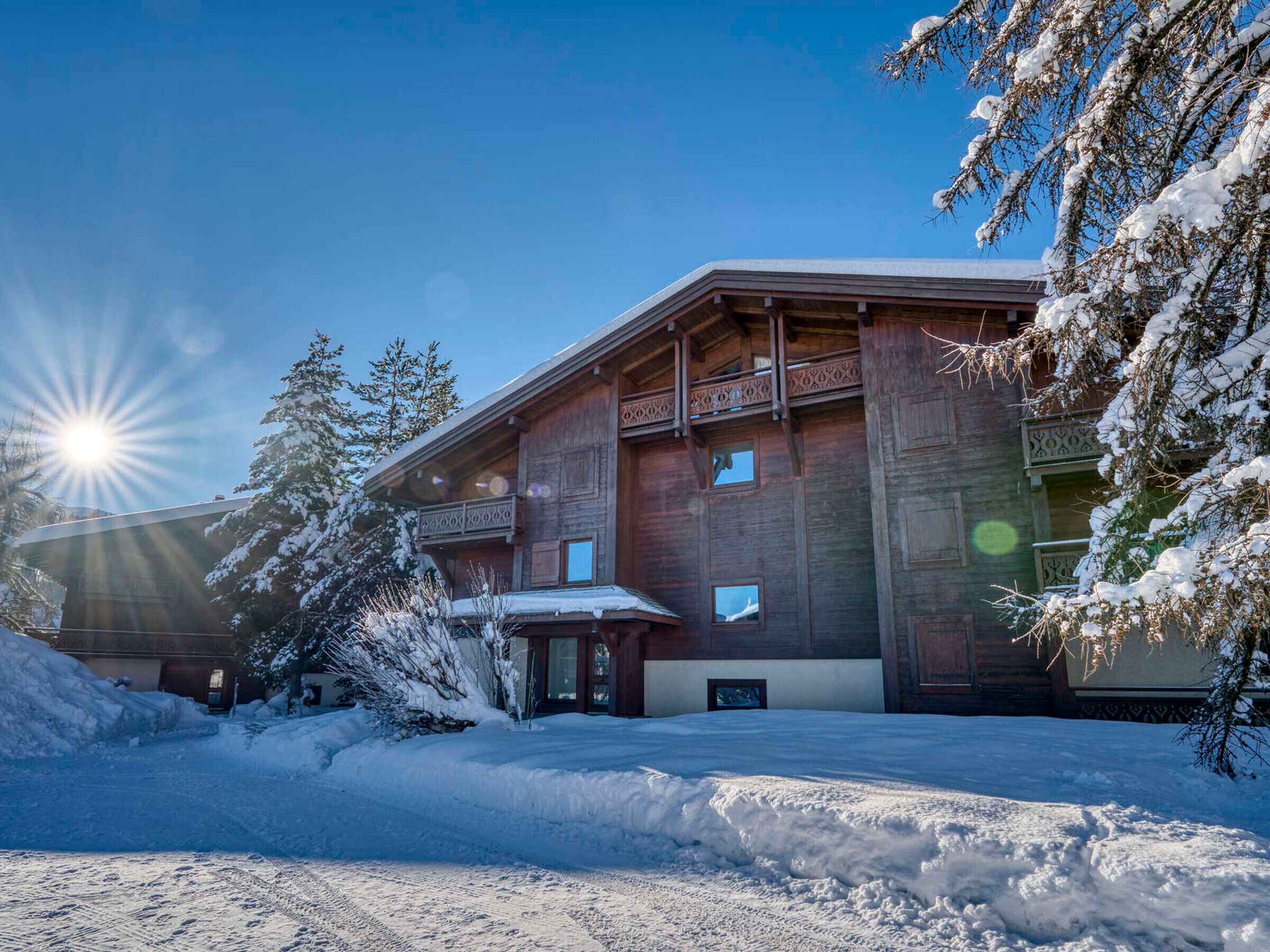 Una cabaña de madera con balcón y ventanas amplias, rodeada de árboles cubiertos de nieve.